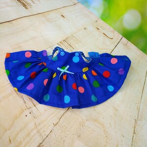 May include: A blue polka dot dress with a ruffled skirt. The dress has colourful polka dots in red, yellow, green, pink, and purple. It features a small blue bow and two buttons at the neckline.
