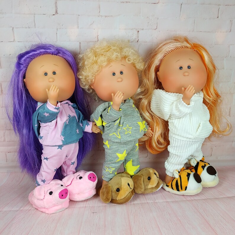 May include: Three dolls with purple, blonde, and orange hair wearing pajamas. The doll with purple hair is wearing pink and grey pajamas with stars. The doll with blonde hair is wearing grey pajamas with stars. The doll with orange hair is wearing white pajamas.