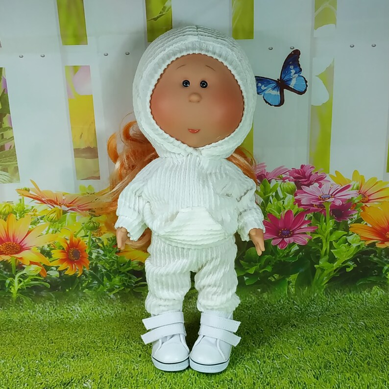 May include: A white doll wearing a white hooded sweatshirt and matching pants. The doll has red hair and large blue eyes.