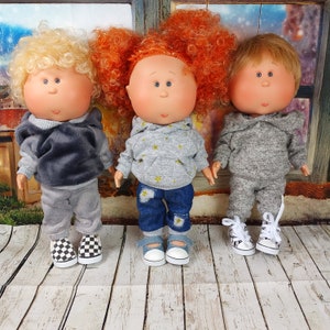 May include: Three handmade dolls with different colored hair and clothing. The dolls are wearing grey hoodies and pants, and one doll is wearing blue jeans. The dolls are standing on a wooden surface.