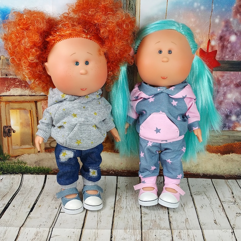 May include: Two handmade dolls with painted faces and colorful hair. One doll is wearing a grey hoodie with stars and blue jeans. The other doll is wearing a pink and grey hoodie with stars and pink and grey pants.