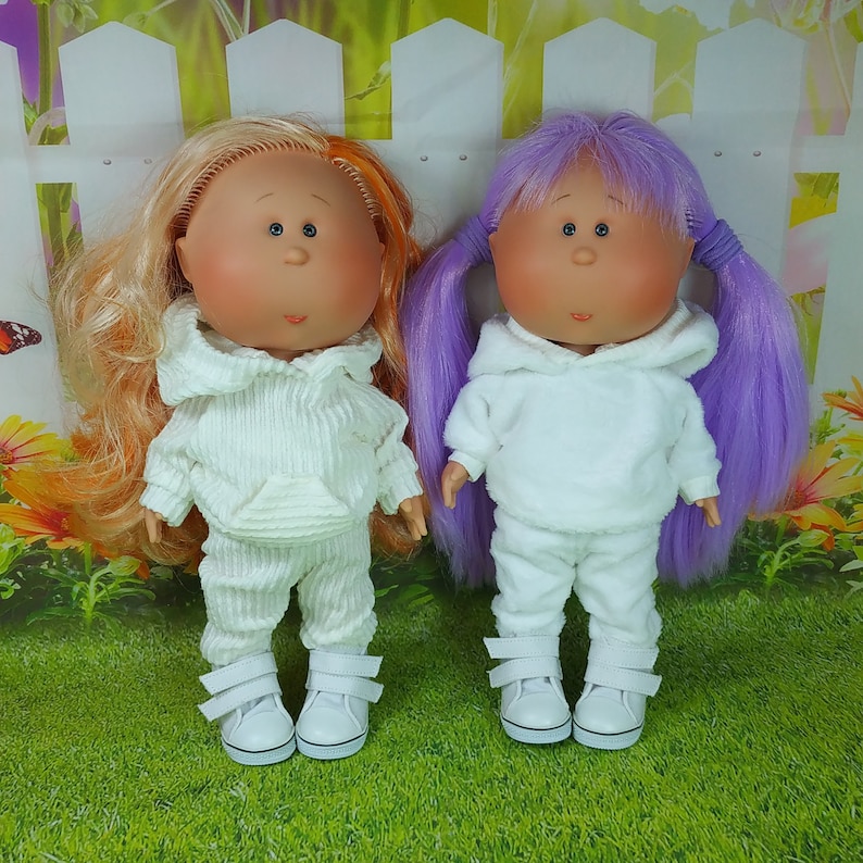 May include: Two dolls with white hooded sweatshirts and matching pants. One doll has orange hair and the other has purple hair.