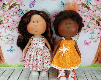May include: Two handmade dolls wearing dresses and sneakers. One doll has brown hair and a floral dress, the other has brown skin and curly brown hair and is wearing an orange dress.