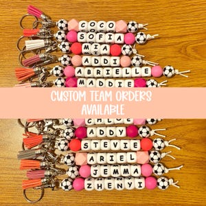 Pu&ograve; includere: Portachiavi con nomi scritti con perline di lettere bianche, intervallati da perline rosa, pesca e pallone da calcio. Ogni portachiavi ha un nappa in vari colori. &Egrave; visibile anche il testo "CUSTOM TEAM ORDERS AVAILABLE".
