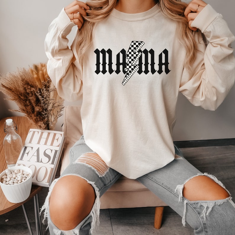 May include: A cream colored long-sleeved sweatshirt with the word "MAMA" in black gothic lettering with a black and white checkered lightning bolt graphic.