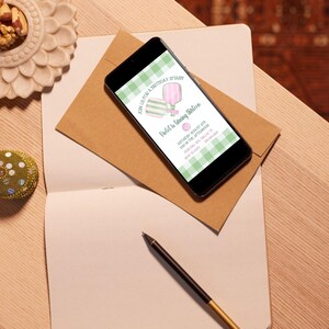 May include: A smartphone displays a birthday party invitation with a green and white gingham pattern. The invitation reads "Join us for a birthday splash! Violet is turning thirteen." The phone rests on a brown envelope, a notebook, and a pen.
