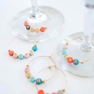 Peut inclure: Quatre charmes &agrave; verre &agrave; vin de couleur or avec des perles color&eacute;es &eacute;pellant les noms "Sydney", "Elena", "Maddie" et "Esmeralda".