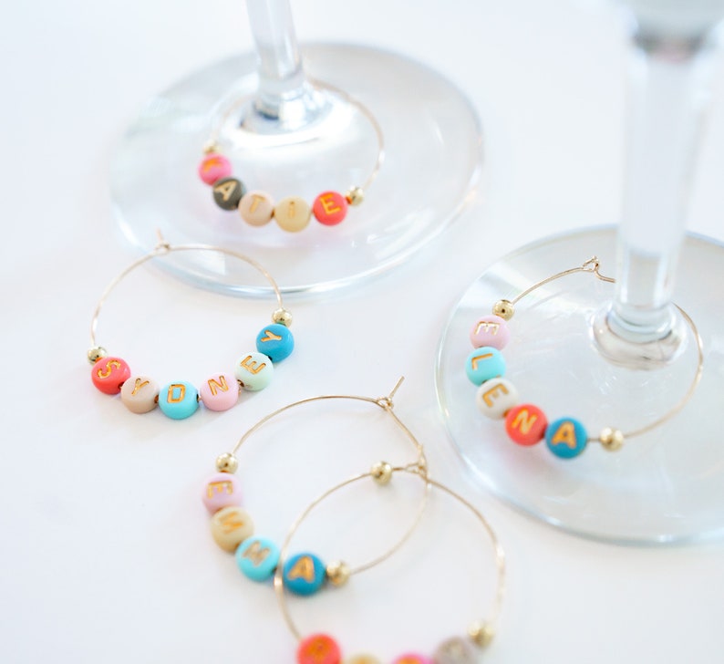 Peut inclure: Quatre charmes &agrave; verre &agrave; vin de couleur or avec des perles color&eacute;es &eacute;pellant les noms "Sydney", "Elena", "Maddie" et "Esmeralda".