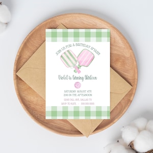May include: A birthday invitation with a green and white gingham border. The invitation reads "Join us for a birthday smash! Violet is turning thirteen." The invitation is on a wooden plate with a brown envelope.
