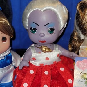 May include: A Precious Moments doll of Ursula from The Little Mermaid. The doll has a purple face, white hair, and a red and white polka dot dress. A gold seashell pendant hangs around her neck. The doll is part of a collection.