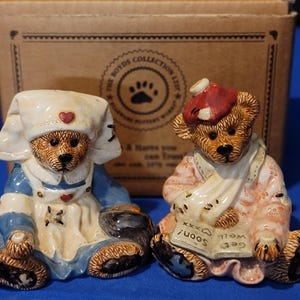 May include: Two Boyd's Collection bear figurines. One is dressed as a nurse in a blue and white uniform, the other is wearing a red compress and a sling. The bears are brown with detailed facial features and are sitting down.