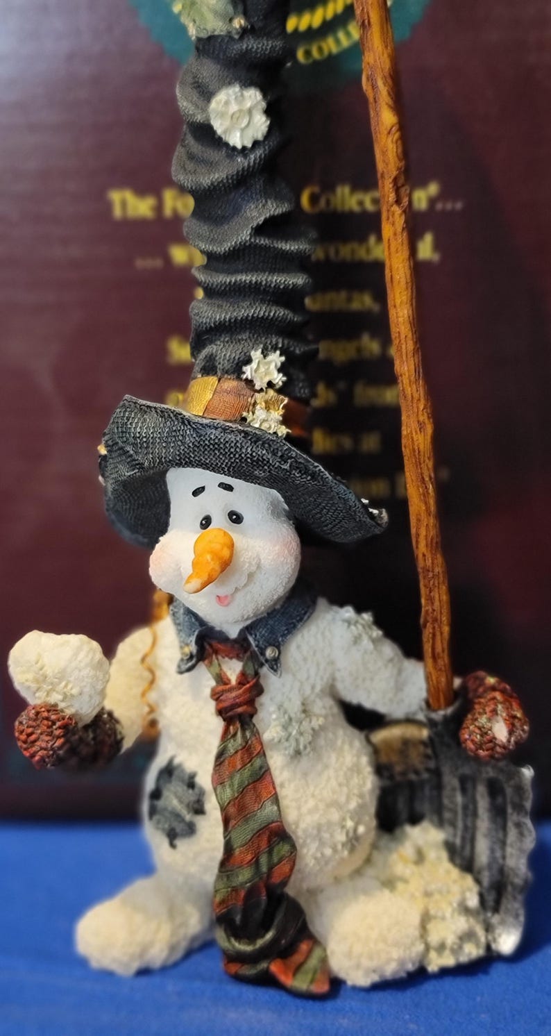 K&ouml;nnte beinhalten: Eine skurrile Schneemannfigur mit schwarzem Hut, Jeansjacke und gestreifter Krawatte. Der Schneemann h&auml;lt einen Besen und einen Schneeball, mit einer Karottennase und einem l&auml;chelnden Gesicht. Sammlerst&uuml;ck.