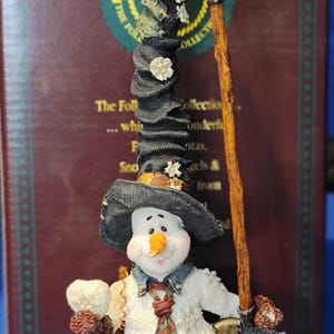 K&ouml;nnte beinhalten: Eine skurrile Schneemannfigur mit einem hohen schwarzen Hut, der mit wei&szlig;en Akzenten verziert ist, und einer passenden Schaufel. Der Schneemann tr&auml;gt eine gemusterte Krawatte und h&auml;lt einen kleinen Gegenstand. Teil der "The Folktales Collection".
