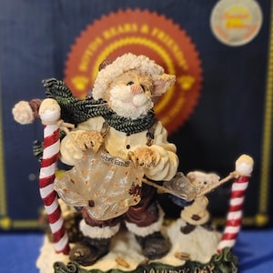 May include: A whimsical figurine of a cat dressed as Santa Claus, holding a sign that says "Wednesday" and a laundry bag. The figurine is on a base that reads "Northpole Laundry Day". The cat is wearing a green scarf and a white hat.