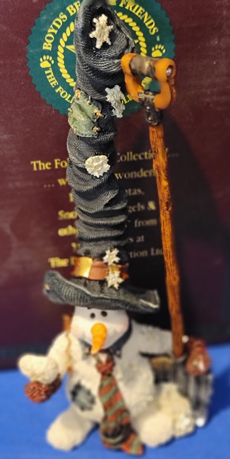K&ouml;nnte beinhalten: Eine skurrile Schneemannfigur mit schwarzem Hut, oranger Karottennase und gestreifter Krawatte. Der Schneemann h&auml;lt einen Besen und ist mit dekorativen Akzenten verziert. Teil einer Sammlung.