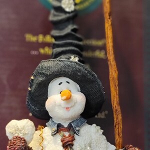 K&ouml;nnte beinhalten: Eine skurrile Schneemannfigur mit schwarzem Hut, bunter gestreifter Krawatte und Jeansjacke. Der Schneemann h&auml;lt eine Schaufel und einen Schneeball. Eine festliche Winterdekoration.