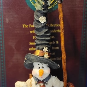 K&ouml;nnte beinhalten: Eine skurrile Schneemannfigur aus der Boyds Collection, die einen schwarzen Hut mit Sternen tr&auml;gt und einen Besen h&auml;lt. Der Schneemann hat eine Karottennase, eine gemusterte Krawatte und einen geflickten Mantel. Die Figur ist ein Sammlerst&uuml;ck.
