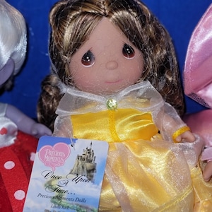 May include: A Precious Moments doll of Belle from Beauty and the Beast. The doll has brown hair, a yellow dress, and a tag that reads "Once Upon a Time..." and "Beauty & the Beast Dreams."