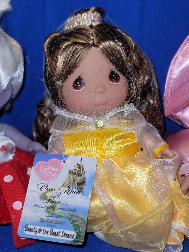 May include: A Precious Moments doll of Belle from Beauty and the Beast. The doll has brown hair, a yellow dress, and a tag that reads "Once Upon a Time..." and "Beauty & the Beast Dreams."