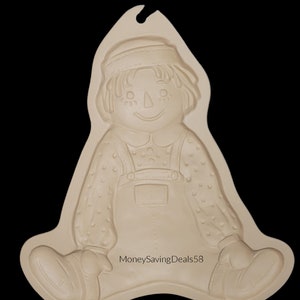May include: A beige, plastic Raggedy Ann doll mold with a smiling face, wearing a bonnet and overalls. The mold has a loop at the top for hanging. The text "MoneySavingDeals58" is printed on the bottom.
