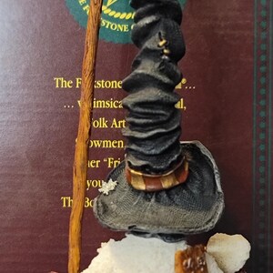 K&ouml;nnte beinhalten: Eine skurrile Schneemannfigur mit schwarzem Hut, die einen Wanderstock und einen Sack h&auml;lt. Der Schneemann hat einen wei&szlig;en K&ouml;rper und einen braunen Rucksack. Die Figur ist ein Volkskunstwerk.
