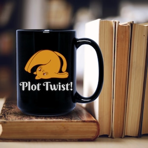May include: Black coffee mug with a white outline of a cat doing a yoga pose and the text "Plot Twist!" printed on it. The mug is sitting on a stack of books.