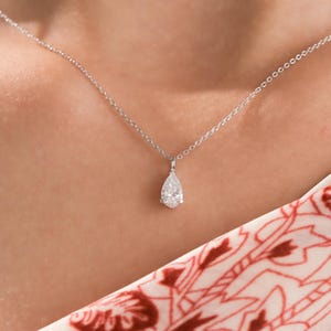 May include: A silver chain necklace with a pear-shaped diamond pendant.