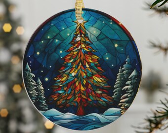 Puede incluir: Un adorno navideño redondo con una ilustración de estilo vitral de un árbol de Navidad colorido con una estrella en la cima, rodeado de una escena invernal azul y blanca.