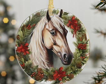 Könnte beinhalten: Ein runder Weihnachtsbaumschmuck aus Glas mit einem Gemälde eines hellbraunen Pferdes mit weißer Mähne und Schweif. Das Pferd ist von einem Kranz aus Kiefernästen, roten Beeren und Weihnachtssternen umgeben.