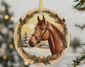 Könnte beinhalten: Runder Weihnachtsbaumschmuck mit einem braunen Pferd mit Zaumzeug vor einer Winterlandschaft mit schneebedeckten Bäumen und einem kleinen Haus. Das Pferd ist von einem Kranz aus immergrünen Zweigen und roten Beeren umrahmt.