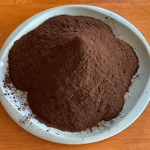 May include: A close-up of a pile of dark brown powder on a light blue plate.