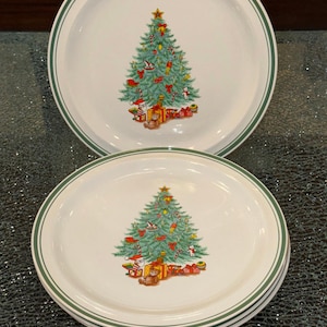 Puede incluir: Platos de cerámica blancos con borde verde y diseño de árbol de Navidad. El árbol está decorado con adornos, una estrella y regalos en la base. Se ve una pila de platos.
