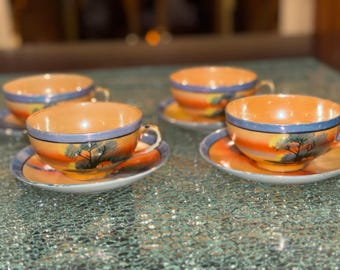 May include: Four vintage teacups and saucers with a colorful sunset and tree design. The cups and saucers are made of porcelain and have a glossy finish.