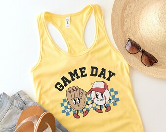 May include: Yellow tank top with a baseball themed graphic that says "GAME DAY". The graphic features a baseball and a baseball glove with cartoon faces.