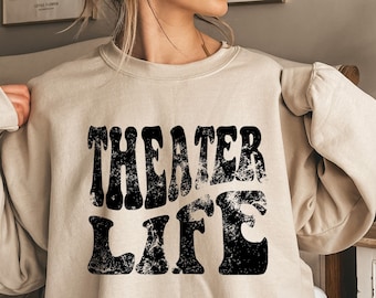 May include: A beige sweatshirt with the text "THEATER LIFE" printed in black, distressed lettering.