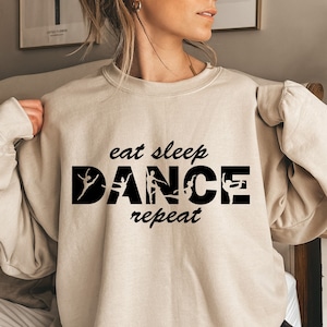 May include: A beige sweatshirt with the text "eat sleep dance repeat" in black. The word "dance" is made up of silhouettes of dancers in different poses.