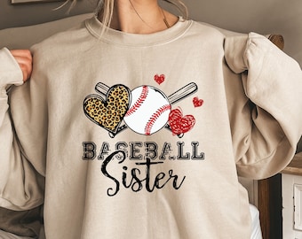 May include: A beige sweatshirt with a baseball, two crossed bats, and a leopard print heart. The text "Baseball Sister" is printed on the sweatshirt.