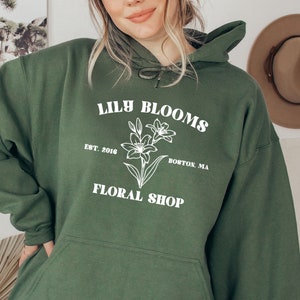 May include: A dark green hooded sweatshirt with the text "Lily Blooms" in white, a floral design, and the text "Est. 2016 Boston, MA Floral Shop".