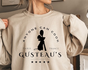 May include: A beige sweatshirt with a black graphic print that says "Anyone can cook Paris Gusteau's France" with a silhouette of a rat holding a spoon.
