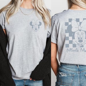 Pu&ograve; includere: Maglietta grigia con un design a scacchi bianco e nero con una grafica di Minnie Mouse grigia e il testo "Minnie Mouse".