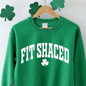 May include: Green sweatshirt with white text that reads "Fit Shaced" and a white shamrock.