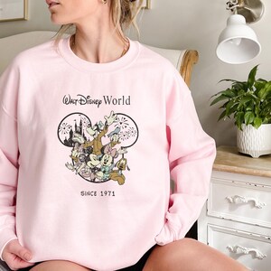 Puede incluir: Sudadera rosa con un gr&aacute;fico de Mickey Mouse y sus amigos frente al Castillo de Cenicienta. El texto "Walt Disney World Since 1971" est&aacute; impreso debajo del gr&aacute;fico.