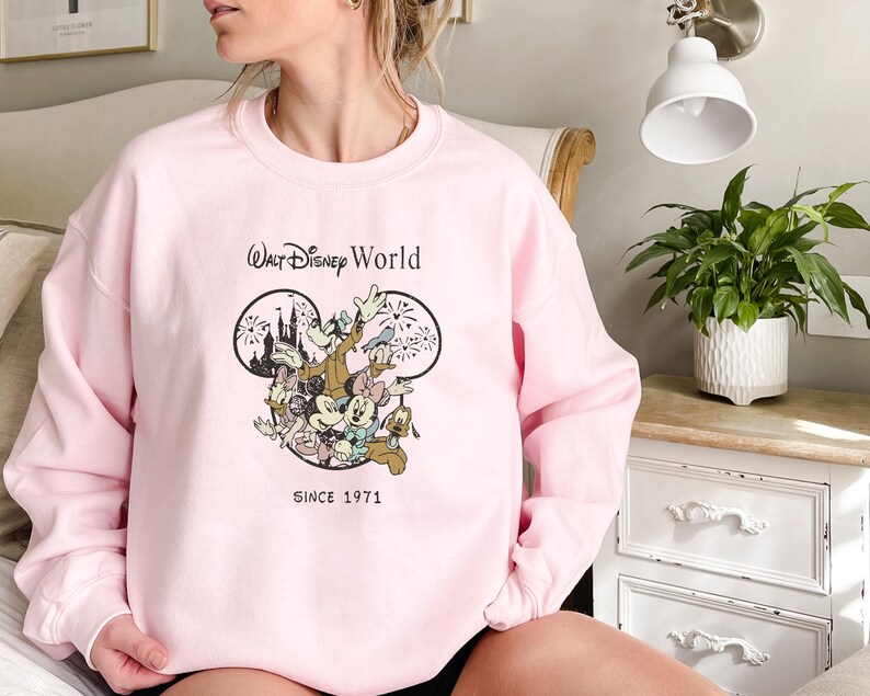 Puede incluir: Sudadera rosa con un gr&aacute;fico de Mickey Mouse y sus amigos frente al Castillo de Cenicienta. El texto "Walt Disney World Since 1971" est&aacute; impreso debajo del gr&aacute;fico.