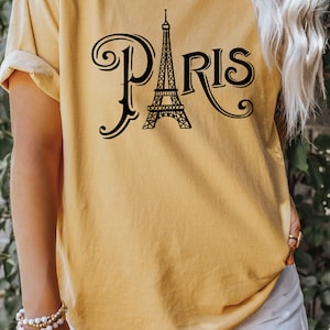 May include: A mustard yellow t-shirt with a black graphic of the Eiffel Tower and the word "PARIS" in a stylized font.