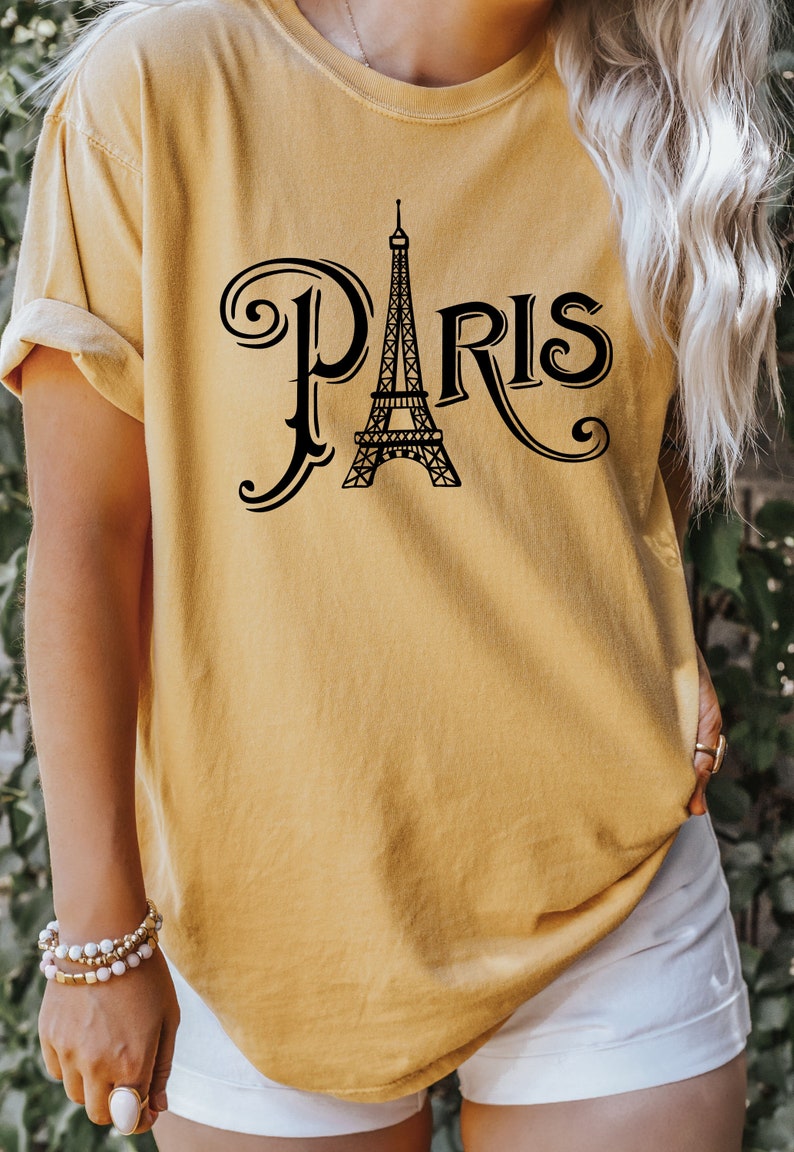 May include: A mustard yellow t-shirt with a black graphic of the Eiffel Tower and the word "PARIS" in a stylized font.