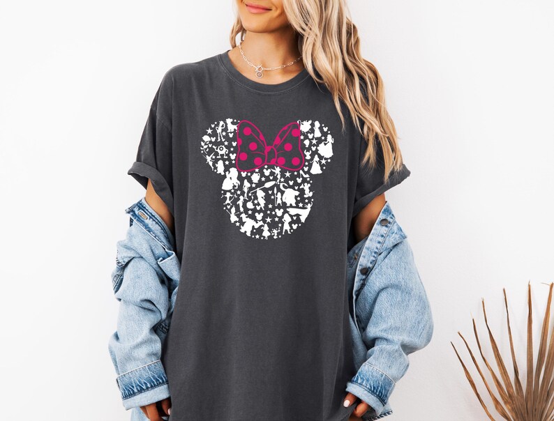 May include: A dark gray t-shirt with a white silhouette of Mickey Mouse's head made up of various Disney characters. The bow on Mickey's head is pink with white polka dots.