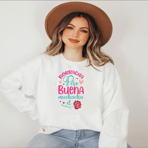 May include: White sweatshirt with a pink and blue graphic design that says "Borracha Pero Buena Muchacha" with a pink rose and stars.