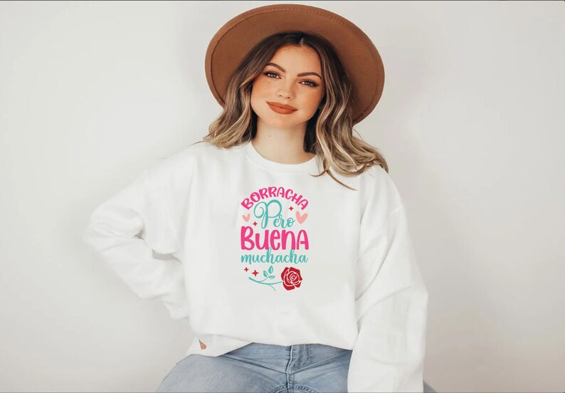May include: White sweatshirt with a pink and blue graphic design that says "Borracha Pero Buena Muchacha" with a pink rose and stars.