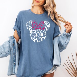 May include: A blue t-shirt with a white silhouette of Mickey Mouse's head made up of various Disney characters. The bow is pink with white polka dots.