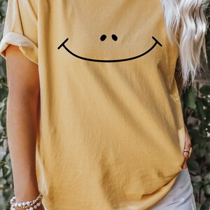 May include: A mustard yellow t-shirt with a black smiley face graphic.